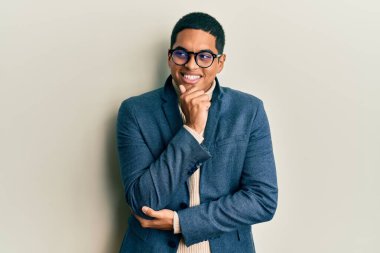 Zarif kıyafetler giyen, eli çenesinde gözlüklü, soru soran, düşünceli bir İspanyol genç. Düşünceli bir yüzle gülümsüyor. şüphe kavramı. 