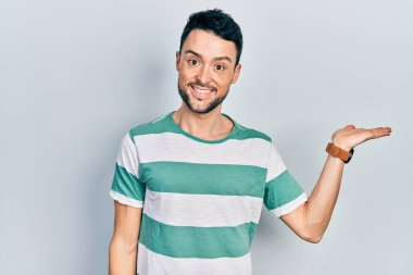 Gündelik kıyafetler giyen genç İspanyol adam neşeli bir şekilde gülümsüyor ve avuç içi kameraya bakıyor.. 