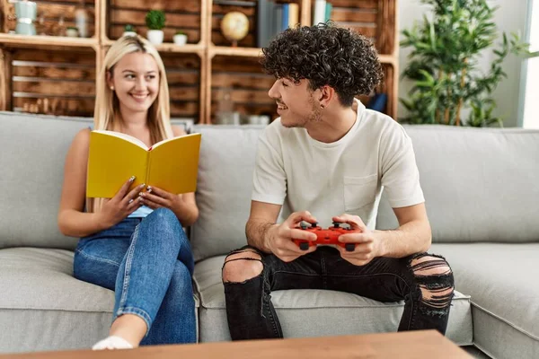 Young Couple Smiling Happy Playing Video Game Reading Book Home — ストック写真