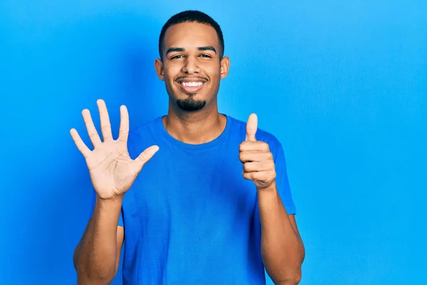 身穿休闲蓝T恤的年轻的非洲裔美国人 带着自信和快乐的笑容 用手指指了指6号 — 图库照片