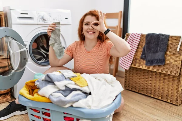 手笑顔で をジェスチャーを行う洗濯機に汚れた洗濯機を入れて若い赤毛の女性 幸せな顔で指を通して見て目 — ストック写真