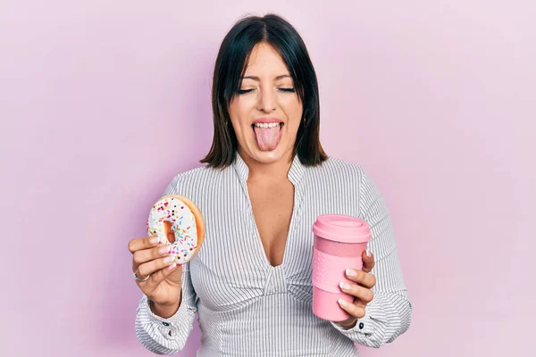 Young Hispanic Woman Eating Doughnut Drinking Coffee Sticking Tongue Out — Stock Photo, Image