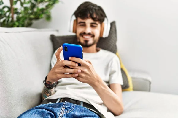 Молодий Іспаномовний Чоловік Використовує Смартфон Навушники Лежать Дивані Вдома — стокове фото