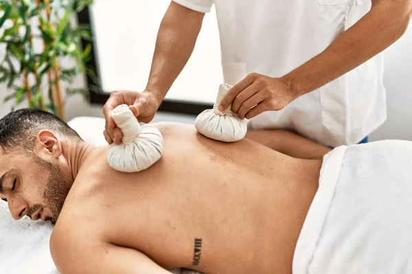 Dos Hombres Hispanos Fisioterapeuta Paciente Masajeando Usando Bolsas Tailandesas Centro —  Fotos de Stock