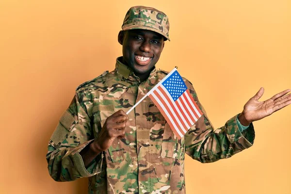 アメリカ軍の制服を着た若いアフリカ系アメリカ人男性が笑顔でアメリカ国旗を掲げ 手を挙げて勝利を祝う — ストック写真