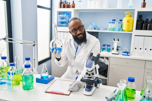 Bilim adamı üniforması giyen genç Afro-Amerikan adam laboratuarda test tüpü tutuyor.