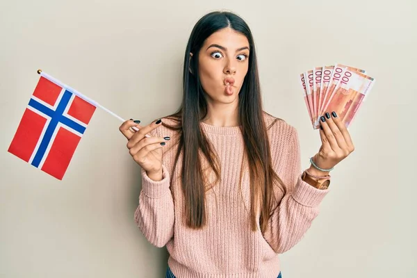 年轻的惊慌失措的女人举着诺威国旗和克朗钞票 用嘴和眼神做鬼脸 疯狂而滑稽 — 图库照片