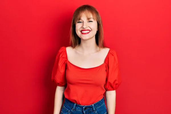 红头发的年轻女人穿着休闲的红色T恤 脸上挂着快乐而凉爽的笑容 幸运的人 — 图库照片
