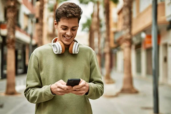 Young hispanic man smiling happy using smartphone and headphones at the city.