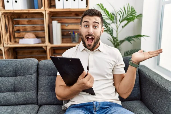 Bonito Homem Hispânico Segurando Prancheta Trabalhando Clínica Psicologia Apontando Para — Fotografia de Stock