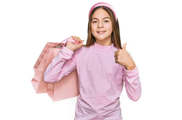 美しいブルネットの女の子を保持ショッピングバッグ笑顔幸せと正 親指アップ行う優れた承認サイン — ストック写真