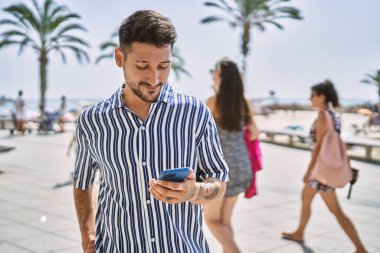 Genç yakışıklı adam deniz kenarında akıllı telefon kullanıyor.