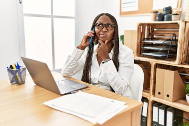 Ofiste örgü ören zenci bir kadın telefonda konuşurken bir soru hakkında endişeli ve gergin bir şekilde konuşuyor. 
