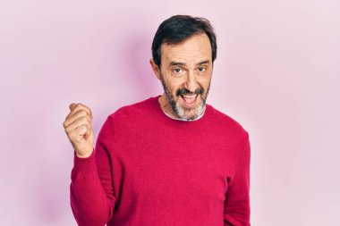 Orta yaşlı İspanyol bir adam, günlük kıyafetler giyiyor, gülümsüyor, gülümsüyor ve başparmağıyla yan tarafa bakıyor.. 