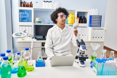 Genç İspanyol adam bilim adamı üniforması giyiyor. Laboratuvarda idrar testi tüpünü inceliyor.