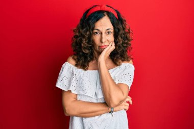 Orta yaşlı İspanyol bir kadın günlük kıyafetler giyip kollarını kavuşturarak depresyondan sıkılmış ve yorgun görünüyor.. 