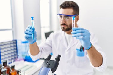 Laboratuvarda deney tüpü tutan bilim adamı üniforması giyen İspanyol genç adam.