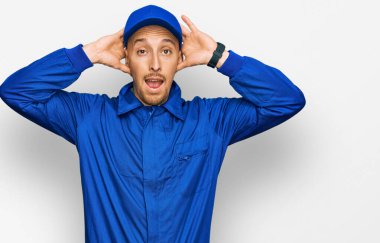 Kel ve sakallı adam, inşaatçı üniforması giyiyor. Deli ve elleri başının üstünde korkmuş, ağzı açık şoktan korkmuş ve şaşırmış. 