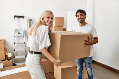 Genç ve güzel bir çift mutlu bir şekilde gülümsüyor. Yeni evlerinde büyük bir karton kutu tutuyorlar..