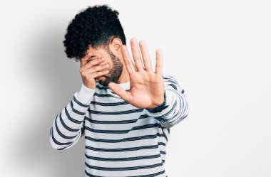 Sakallı, sıradan çizgili süveter giyen, elleriyle gözlerini kapatan, üzgün ve korku dolu hareketler yapan genç bir Arap. utangaç ve olumsuz kavram. 