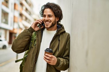 Yakışıklı İspanyol adam telefonda konuşuyor. Duvara yaslanıyor.