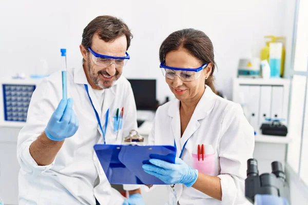 中年男人和女人穿着科学家制服在实验室的剪贴板上写着测试试管 — 图库照片