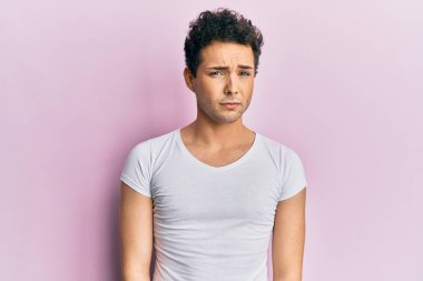 Gündelik beyaz tişört giyen, kuşkucu ve gergin genç yakışıklı bir adam sorun yüzünden surat asıyor. negatif kişi. 