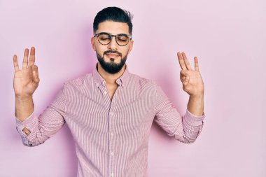 Sakallı, rahat gömlekli ve gözlüklü yakışıklı. Gözleri kapalı gülümseyen, parmaklarıyla meditasyon yapan. yoga konsepti. 