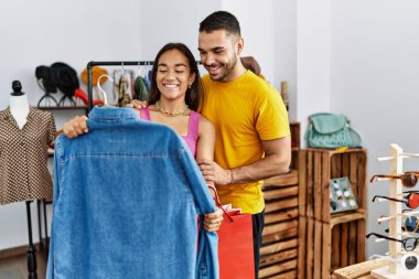 Genç Latin çift gülümsüyor, mağazadan kıyafet seçerken mutlular..