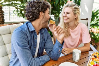 Genç çift, mutlu bir şekilde gülümsüyor. Kahvaltıyı terasta yapıyorlar..