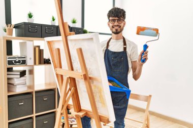 Genç İspanyol ressam mutlu bir resim çiziyor. Resim stüdyosunda boya rulosu kullanıyor..