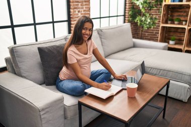 Evde dizüstü bilgisayar kullanarak hamile kalan genç Latin bir kadın.