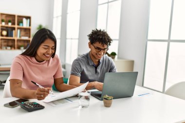 Genç Latin çift evde masada dizüstü bilgisayar kullanarak çalışıyor..