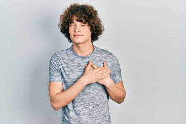 Yakışıklı, gri tişört giyen, elleri göğsünde gülümseyen, gözleri kapalı, yüzünde minnet ifadesi olan genç bir adam. sağlık kavramı. 