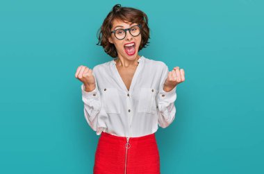 İş stili ve gözlük takan genç İspanyol kadın kollarını kaldırıp, gözlerini açarak başarıyı kutluyor ve şaşırıyor. Kazanan konsept. 