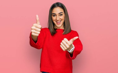 Güzel esmer kadın, sıradan bir kazak giyiyor. Elleriyle olumlu bir jest yapıyor. Gülümsüyor ve başarı için seviniyor. kazanan jest. 