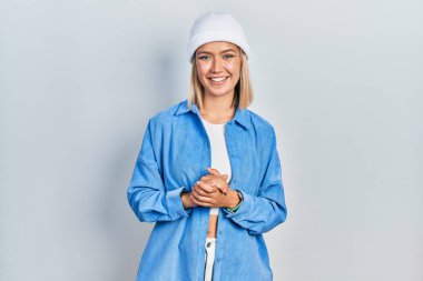 Güzel sarışın kadın yün şapkalı ve elleri çapraz parmaklı rahat ve neşeli gülümsüyor. Başarı ve iyimserlik 