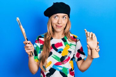 Beyaz kadın sanatçı elinde küçük ahşap manikin ve boya fırçaları ile yan tarafa bakıp düşüncelere daldı.. 