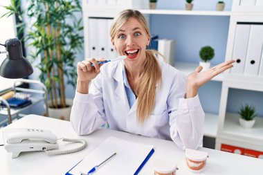 Güzel dişçi kadın diş fırçasıyla diş fırçasını nasıl fırçalayacağını anlatıyor başarıyı mutlu bir gülümsemeyle kutluyor ve kazanan yüz ifadesini kaldırıyor. 