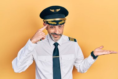 Gri saçlı, uçak pilotu üniforması giyen yakışıklı, kafası karışmış ve avuç içi açık, fotokopi alanı gösteren ve alnını işaret eden orta yaşlı bir adam. Bunu bir düşün.. 