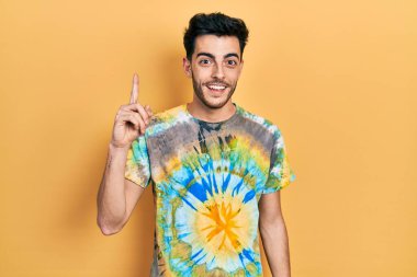 Gündelik kıyafetler giyen genç İspanyol adam başarılı bir fikirle işaret ediyor. Heyecanlı ve mutlu. Bir numara.. 