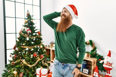 Kızıl saçlı, uzun sakallı, Noel ağacından bir şapka takan, kendine güvenen, el hareketleriyle saçlarına dokunan, çekici ve modaya uygun poz veren bir adam. 