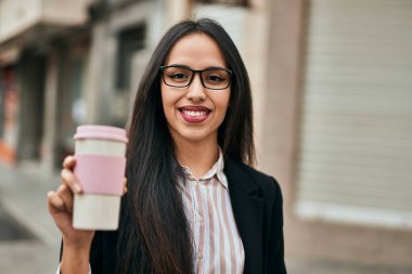 Genç İspanyol iş kadını gülümseyerek şehirde kahveyi yudumluyor..