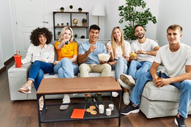 Mutlu bir şekilde gülümseyen bir grup genç arkadaş evde film izliyor..