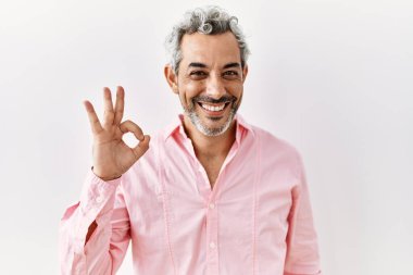 Orta yaşlı İspanyol bir adam izole edilmiş arka planda durup gülümsüyor ve el ve parmaklarıyla 