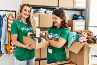 İki genç gönüllü kadın, hayır kurumunda bağışlanacak yiyeceklerle birlikte mutlu bir şekilde kutuda gülümsüyor..