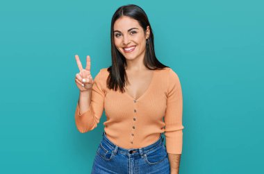 Genç İspanyol kadın gündelik giysiler giyiyor. İki numarayı gösterip işaret ediyor. Kendinden emin ve mutlu bir şekilde gülümsüyor.. 