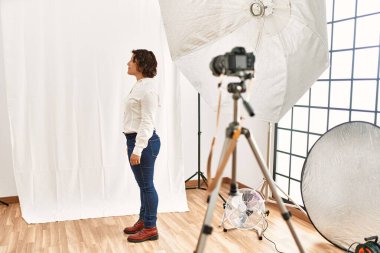 Orta yaşlı İspanyol kadın fotoğraf stüdyosunda mankenlik yapıyor. Tarafsız görünmeye çalışıyor. Profil pozu veriyor.. 