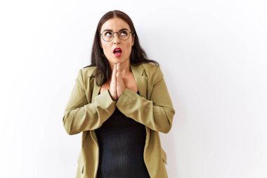 Genç esmer kadın izole edilmiş arka planda duruyor. Elleriyle yalvarıyor ve dua ediyor. Yüzünde umut ifadesi var. Yalvarıyor. 