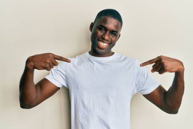 Genç Afro-Amerikan adam, günlük beyaz tişört giyiyor. Kendine güvenen, yüzünde gülümseme olan, kendini gururlu ve mutlu bir şekilde gösteren.. 